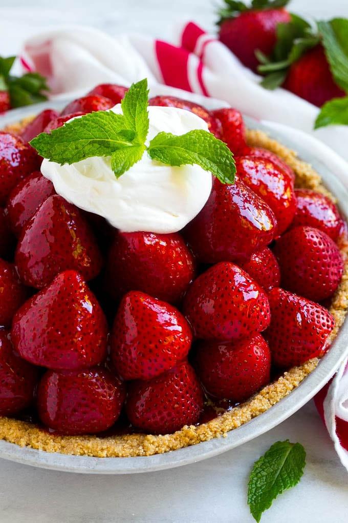 No-Bake Erdbeerkuchen Rezept | Frischer Erdbeerkuchen | Erdbeerkuchen Rezept | No-Bake Kuchen Rezept #erdbeere #erdbeerkuchen #ohnebacken #nobakekuchen #dessert #ahurt Erdbeerkuchen mit einem Haufen frischer Erdbeeren in einem Graham Cracker Boden, bedeckt mit Glasur und Schlagsahne.