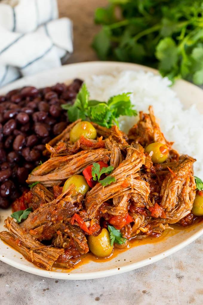 Dieses Ropa Vieja Rezept ist ein traditionelles Gericht aus Rinderbraten, das mit Tomaten und Gewürzen zart geschmort, dann zerzupft und mit Oliven serviert wird. Ein Teller Ropa Vieja serviert mit Reis und schwarzen Bohnen.