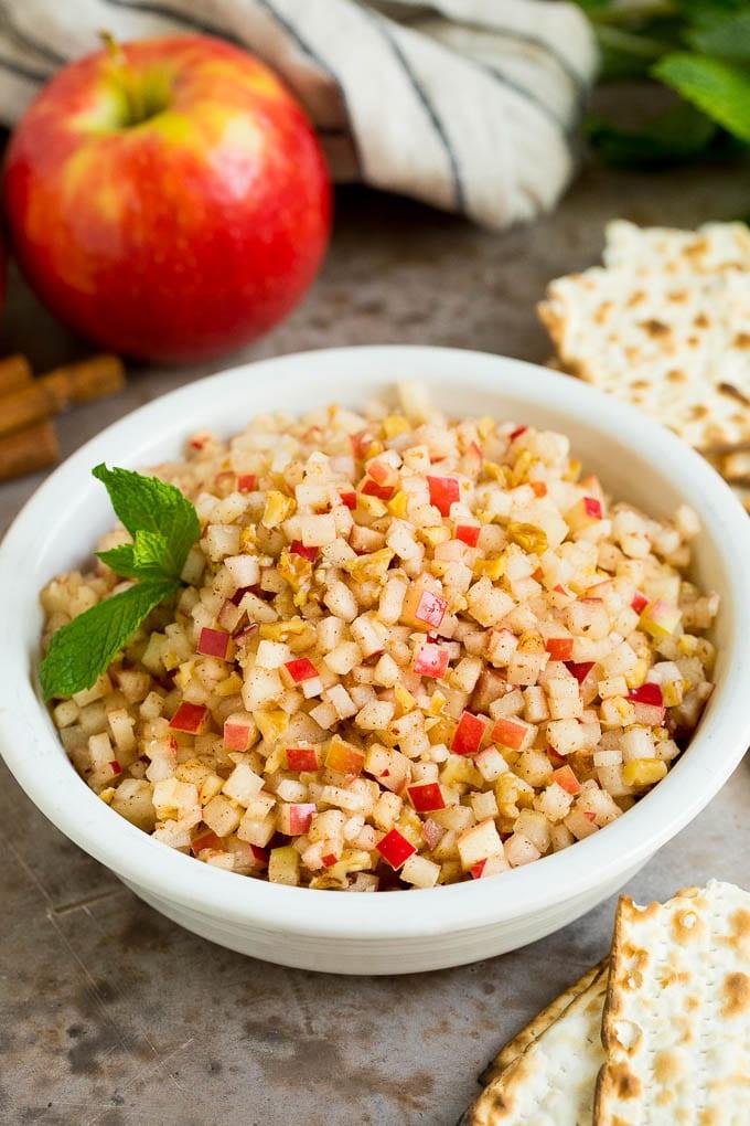 Dieses Charoset Rezept ist eine Mischung aus Äpfeln, Walnüssen und Honig, die zusammen eine süße Paste bilden, die ein wesentlicher Bestandteil jeder Passah-Mahlzeit ist. Eine Schale Charoset, serviert mit Matze und mit Minze garniert.