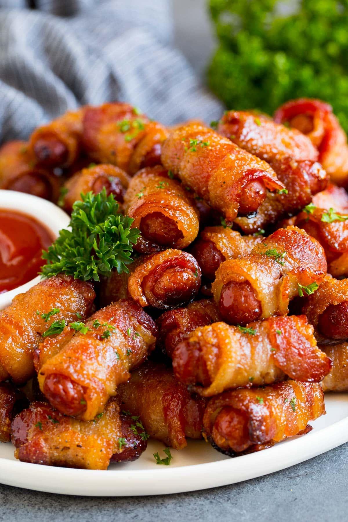 **Würstchen im Speckmantel** 2 Eine Servierplatte mit Bacon Wrapped Smokies, garniert mit Petersilie und einer Beilage Ketchup.