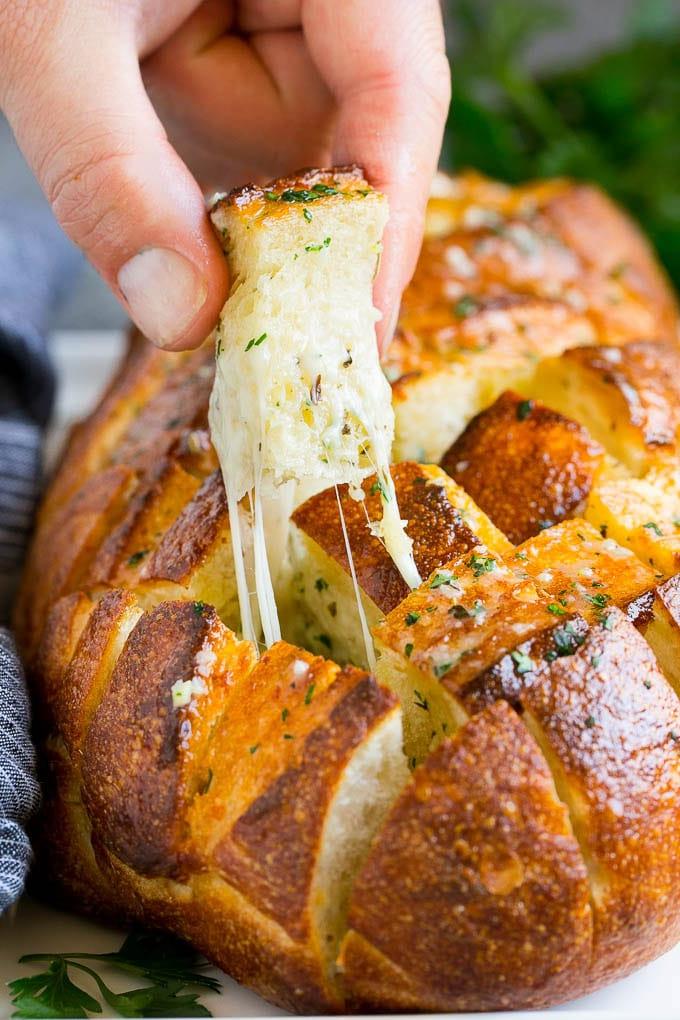 Zupfbrot | Knoblauchbrot | Käsebrot #brot #knoblauch #käse #beilage #vorspeise #ahurt Eine Hand nimmt ein Stück Zupfbrot.