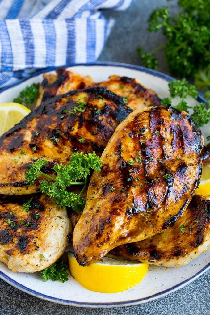 Die beste Hähnchenmarinade, die gegrillte Hähnchenbrüste bedeckt und mit Zitrone garniert ist.