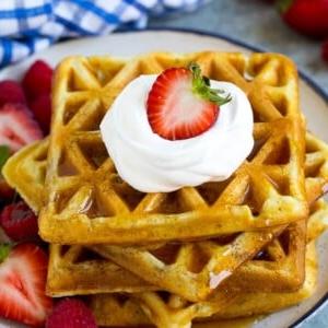 Ein Stapel Buttermilchwaffeln, belegt mit Sirup, Schlagsahne und frischem Obst.
