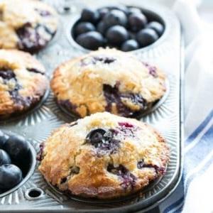 Gesunde Blaubeermuffins in einem Muffinblech mit frischen Blaubeeren als Garnitur.