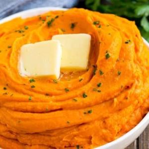 Eine Schüssel Süßkartoffelpüree, belegt mit Butter und Petersilie.