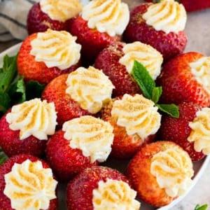 Ein Teller mit mit Käsekuchen gefüllten Erdbeeren, garniert mit frischer Minze.