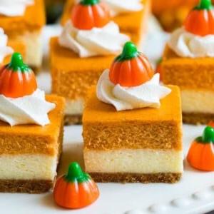 Eine Platte mit Kürbis-Käsekuchenriegeln, belegt mit Schlagsahne und Kürbisbonbons.