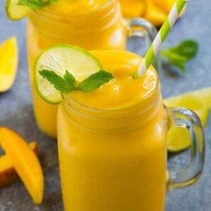 Mango-Smoothie in einem Becher, belegt mit einer Limettenscheibe und einem Minzzweig.