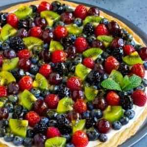 Fruchtpizza mit Zuckerkeksboden und Frischkäse-Frosting, belegt mit Beeren, Kiwi und Trauben.