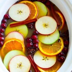 Slow Cooker Apfelwein, garniert mit Apfelscheiben, Orangen, Preiselbeeren, Zimtstangen und Gewürzen.