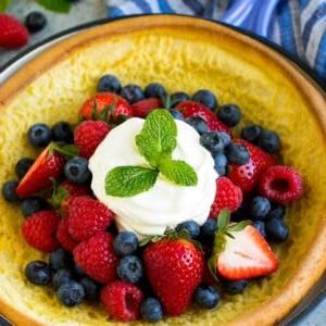 Ein Dutch Baby aufgeblähter Pfannkuchen in einer Pfanne, belegt mit Beeren und Schlagsahne.