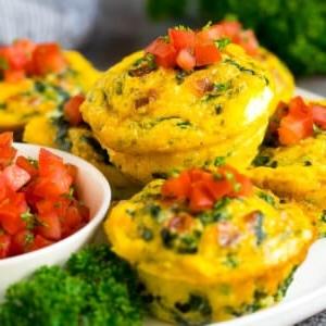 Frühstücks-Eier-Muffins auf einer Servierplatte, garniert mit Tomate und Kräutern.