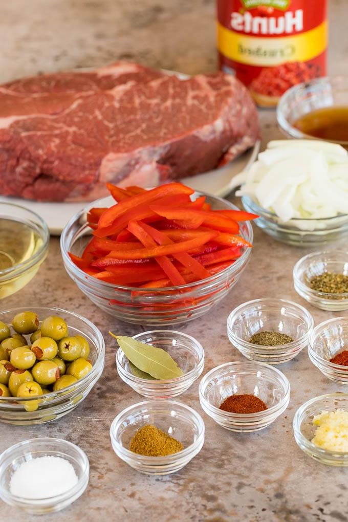 Dieses Ropa Vieja Rezept ist ein traditionelles Gericht aus Rinderbraten, das mit Tomaten und Gewürzen zart geschmort, dann zerzupft und mit Oliven serviert wird. Zutaten in Glasschalen, darunter Zwiebeln, Paprika, Oliven und Gewürze.