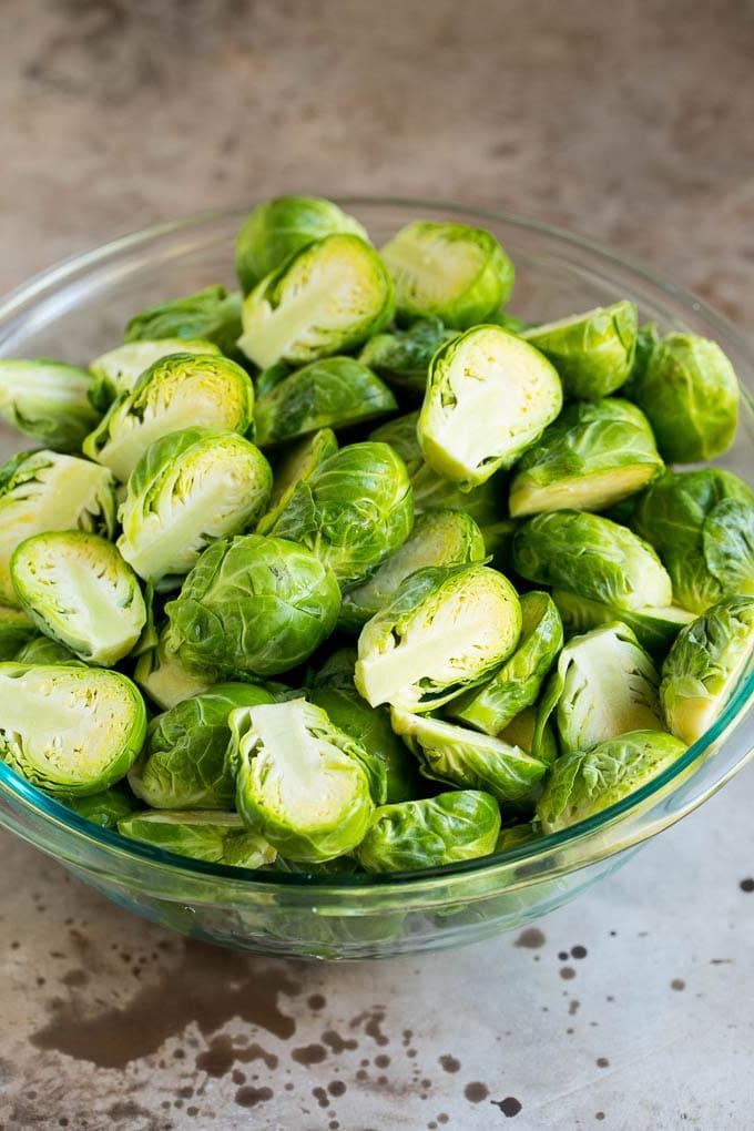 Dieser knusprige Rosenkohl ist mit Olivenöl, Knoblauch und Gewürzen überzogen und wird bei hoher Hitze geröstet, bis er zart und goldbraun ist. Halbierte Rosenkohlröschen in einer Schüssel, bereit für die Würzung mit Olivenöl, Knoblauch und Gewürzen.