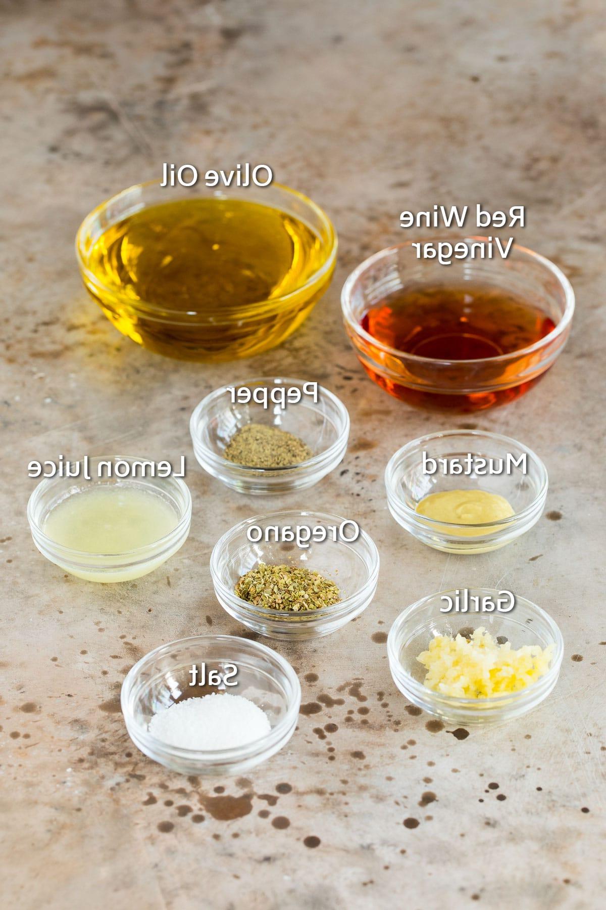 Griechisches Salatdressing 3 Schalen mit Zutaten wie Olivenöl, Rotweinessig, Zitronensaft, frischem Knoblauch und verschiedenen Gewürzen für ein griechisches Dressing.