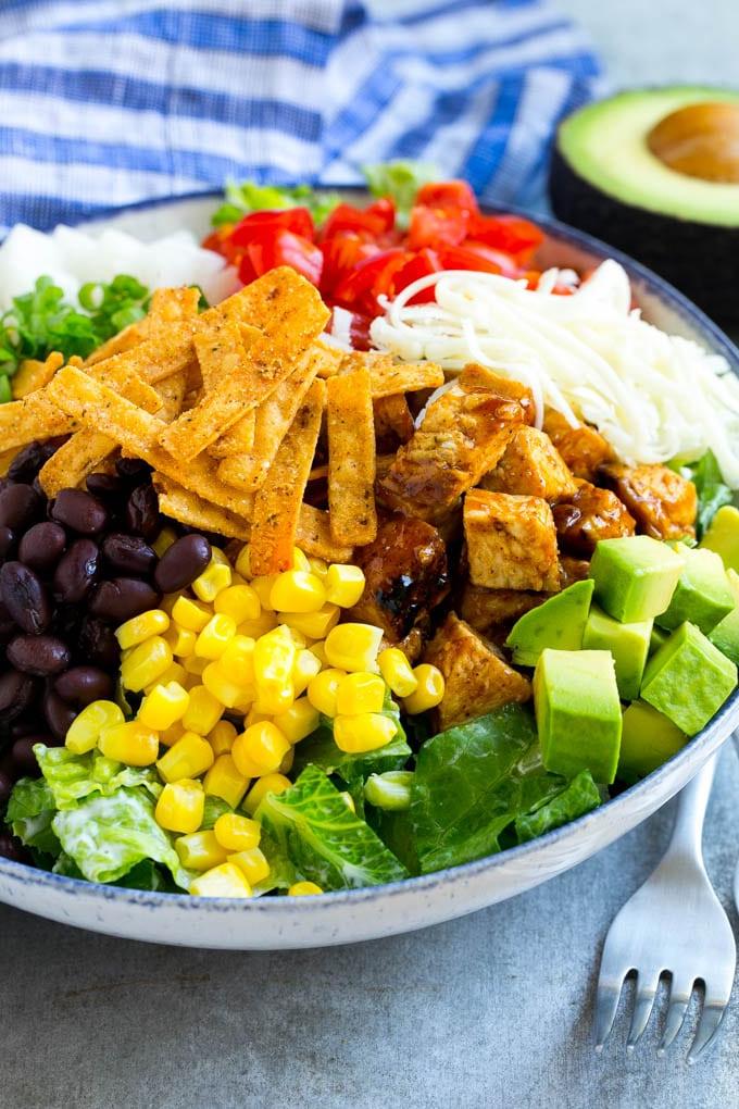 BBQ Hähnchen Salat Rezept | Gehackter BBQ Hähnchen Salat | CPK Copycat Rezept | California Pizza Kitchen Copycat Rezept | Hähnchen Ranch Salat #copycat #CPK #BBQchicken #chicken #salad #dinner #ahurt Eine Schüssel Salat, belegt mit Hähnchen, Tortillastreifen, schwarzen Bohnen, Jicama, Avocado und Tomaten.