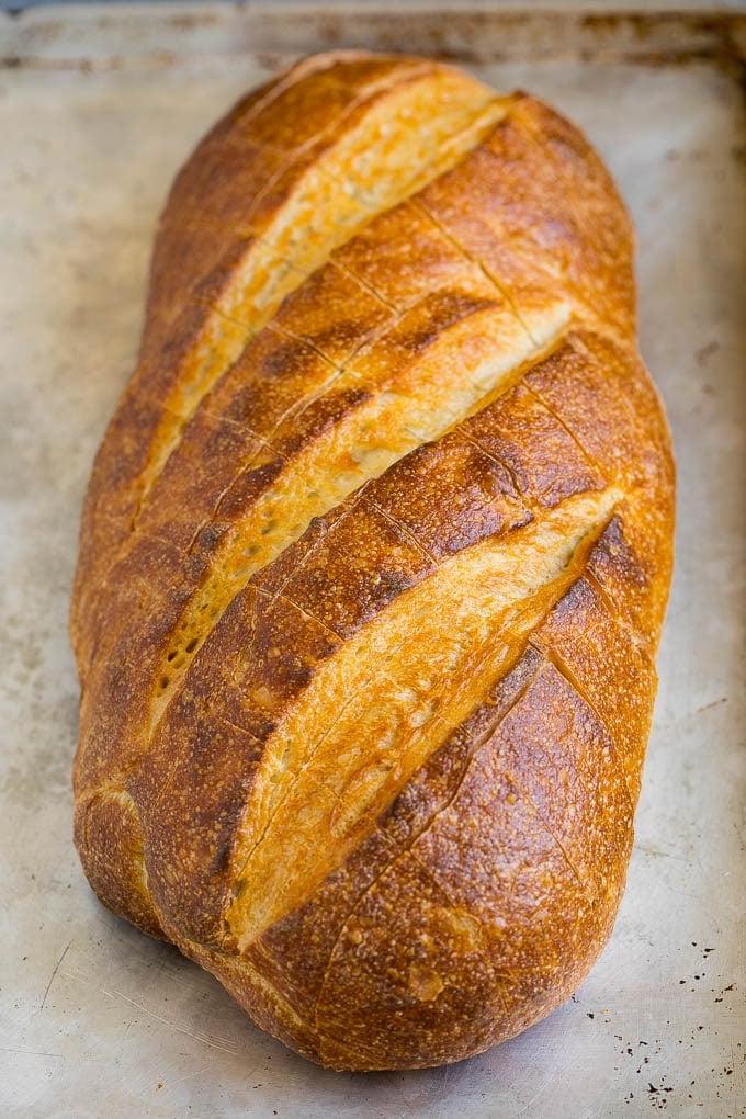 Zupfbrot | Knoblauchbrot | Käsebrot #brot #knoblauch #käse #beilage #vorspeise #ahurt Ein Brotlaib auf einem Backblech mit diagonalen Einschnitten.