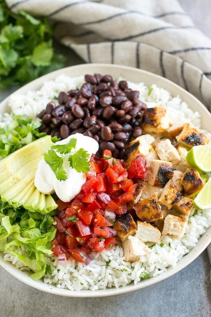 Burrito Bowls mit Reis, Hähnchen, Salsa, Bohnen und Avocado angerichtet.