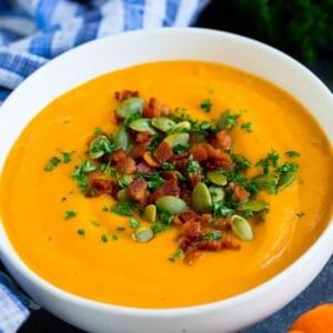 Eine Schüssel Kürbiscremesuppe, belegt mit Speck und Kürbiskernen.