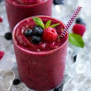 Ein Glas gefrorener Frucht-Smoothie in zerstoßenem Eis, garniert mit Beeren und Minze.