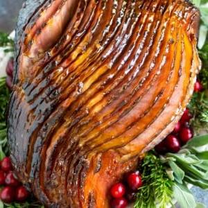 Ein glasierter Schinken auf einer Platte mit Kräutern und Cranberries.