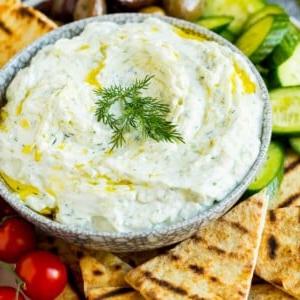 Eine Schale Tzatziki, serviert mit Pitabrot und Gemüse.