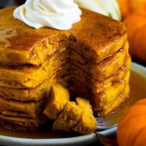 Ein Stapel Kürbispfannkuchen mit einer Gabel, die geschnittene Stücke Pfannkuchen hält.