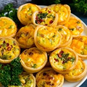 Ein Teller Mini-Quiche, gefüllt mit Fleisch, Gemüse und Käse.