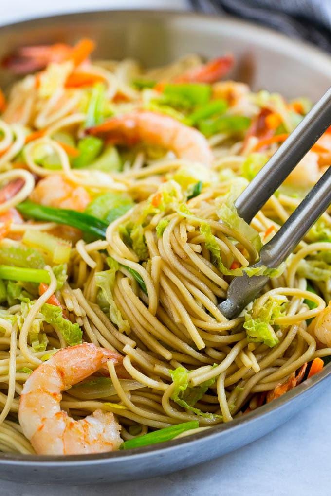 Garnelen Chow Mein Rezept | One-Pot Garnelen Chow Mein | Bestes Garnelen Chow Mein | Einfaches Garnelen Chow Mein | One-Pot Chow Mein #asiatisch #chowmein #garnelenchowmein #onepotmeal #asiatischenudeln #abendessen #abendessenzuHause Eine Pfanne voller Garnelen Chow Mein Nudeln, wobei eine Zange Nudeln heraushebt.