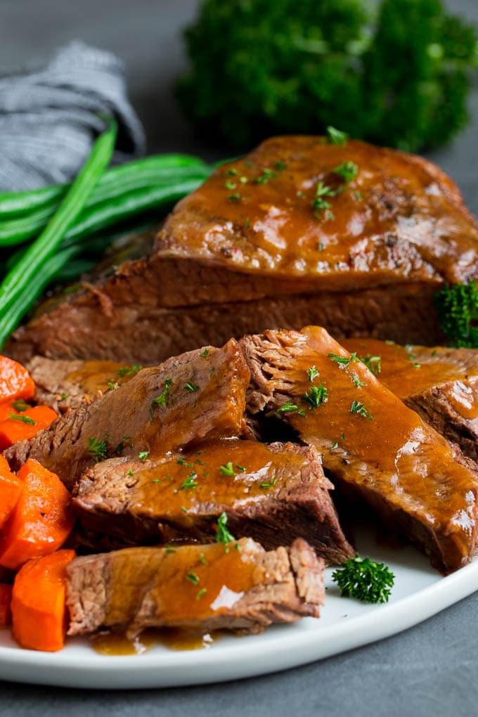 Aufgeschnittene Slow Cooker Rinderbrust mit Sauce und Gemüse serviert.
