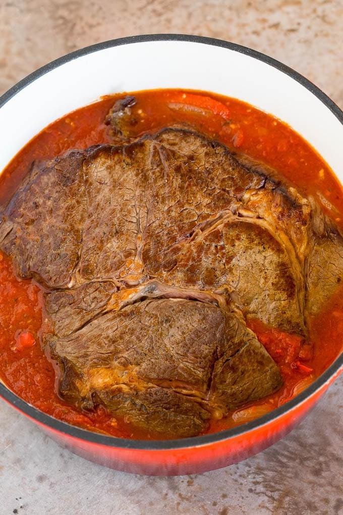Dieses Ropa Vieja Rezept ist ein traditionelles Gericht aus Rinderbraten, das mit Tomaten und Gewürzen zart geschmort, dann zerzupft und mit Oliven serviert wird. Ein angebratener Braten in einem Topf mit Tomaten- und Pfeffersauce.