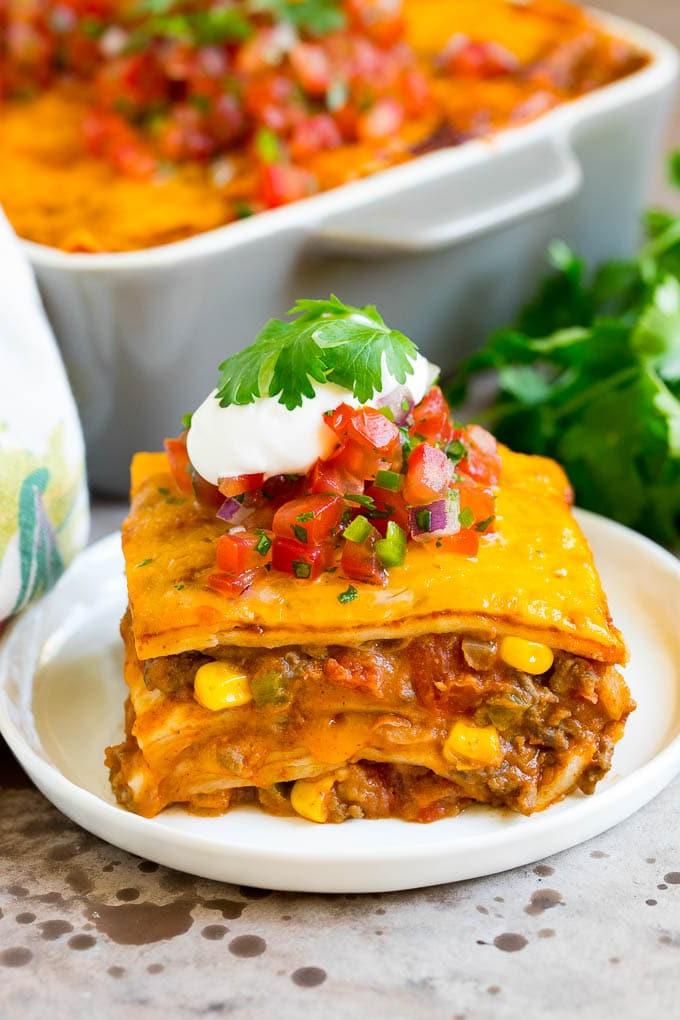 Eine Scheibe Taco-Lasagne garniert mit Salsa, Sauerrahm und Koriander.