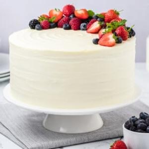 Ein Berry Chantilly Kuchen auf einer Tortenplatte, dekoriert mit frischen Beeren und Minzblättern.