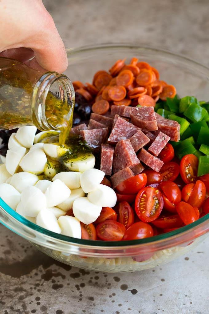 Italienischer Nudelsalat | Nudelsalat Rezept #Nudeln #Salat #Nudelsalat #Peperoni #Salami #Oliven #Käse #Beilage #Abendessen Italienisches Dressing wird über Nudelsalat-Zutaten gegossen.