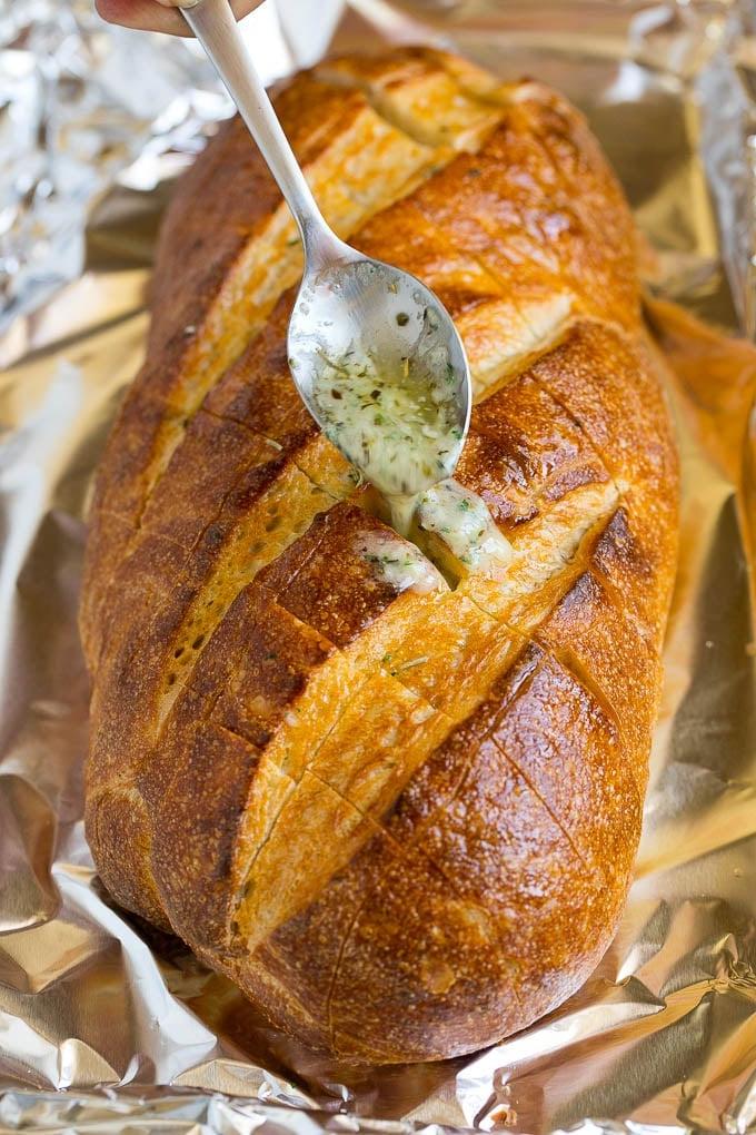 Zupfbrot | Knoblauchbrot | Käsebrot #brot #knoblauch #käse #beilage #vorspeise #ahurt Ein Löffel träufelt Knoblauchbutter über einen Brotlaib.