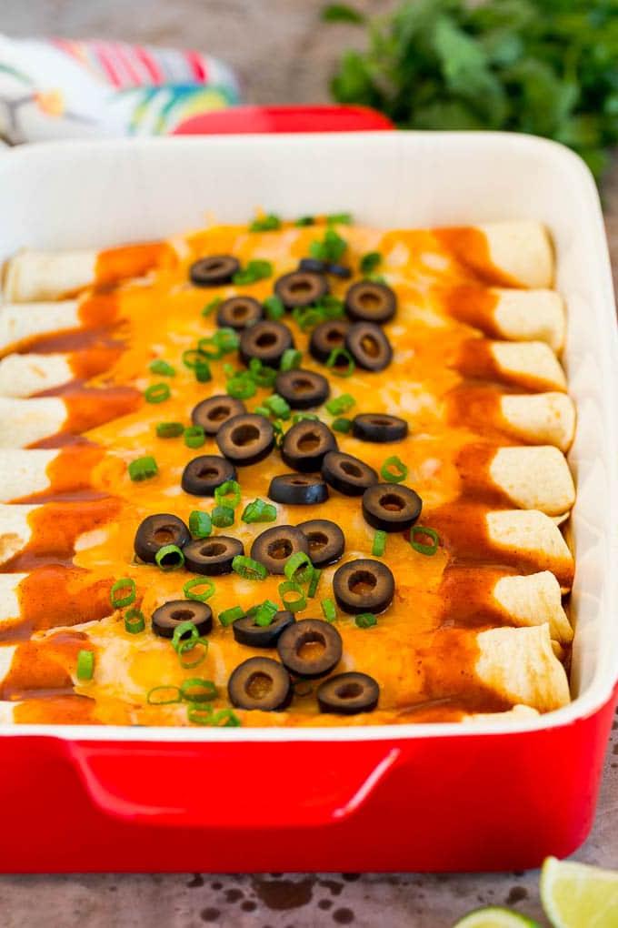 Eine Auflaufform mit Käse-Enchiladas, garniert mit schwarzen Oliven und grünen Zwiebeln, servierfertig.