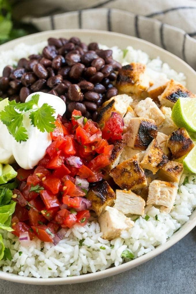 Eine Burrito Bowl mit gegrilltem Hähnchen, Salsa, Avocado, Sauerrahm, schwarzen Bohnen und Reis appetitlich angerichtet.