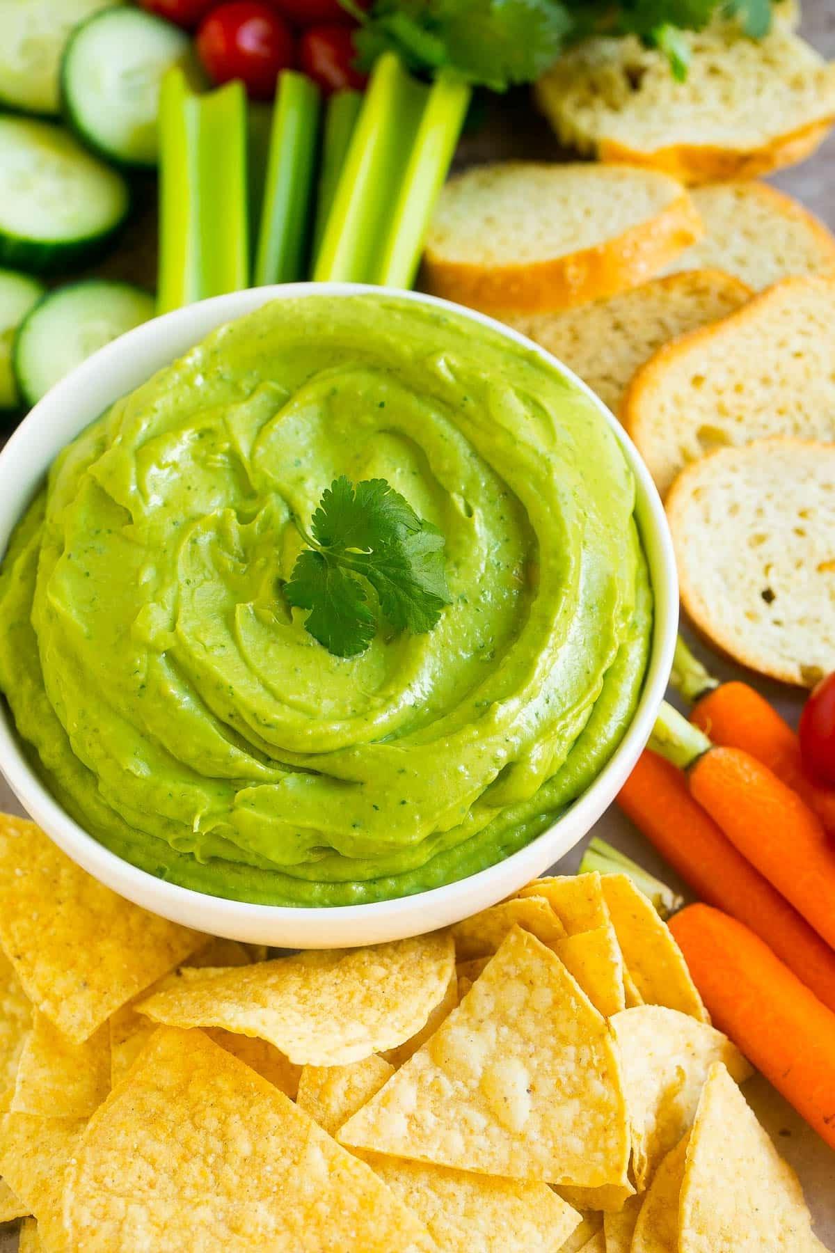 Eine Schüssel Avocado-Dip umgeben von Chips und Gemüse.