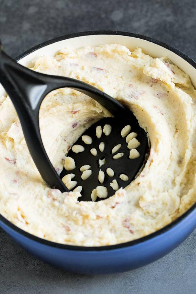 Diese Kartoffelpüree aus roten Kartoffeln sind zarte Kartoffeln, kombiniert mit Knoblauch, Butter und Gewürzen, um eine einfache und doch völlig befriedigende Beilage zu schaffen. Ein Kartoffelstampfer in einem Topf mit Kartoffeln.