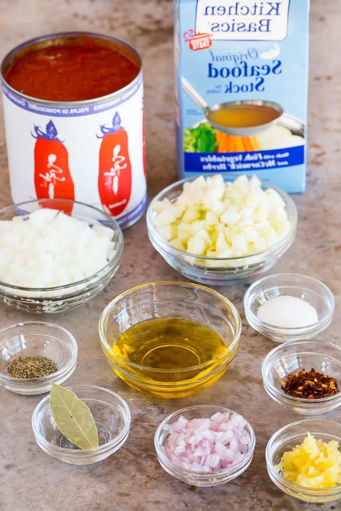 Bereits abgemessene Zutaten in kleinen Schüsseln, darunter frisches Gemüse, hochwertiges Olivenöl und aromatische Gewürze, akkurat für die Cioppino-Zubereitung vorbereitet.