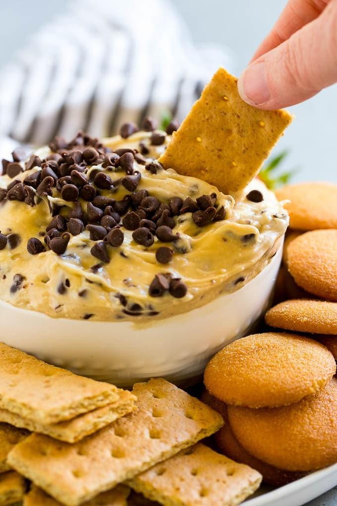 Cookie Dough Dip Rezept | Essbarer Cookie Dough | Schoko-Chip-Keks-Dip #cookies #dip #cookiedough #dessert #snack #ahurt Ein Graham Cracker, der in eine Schüssel mit Cookie Dough Dip getaucht wird.