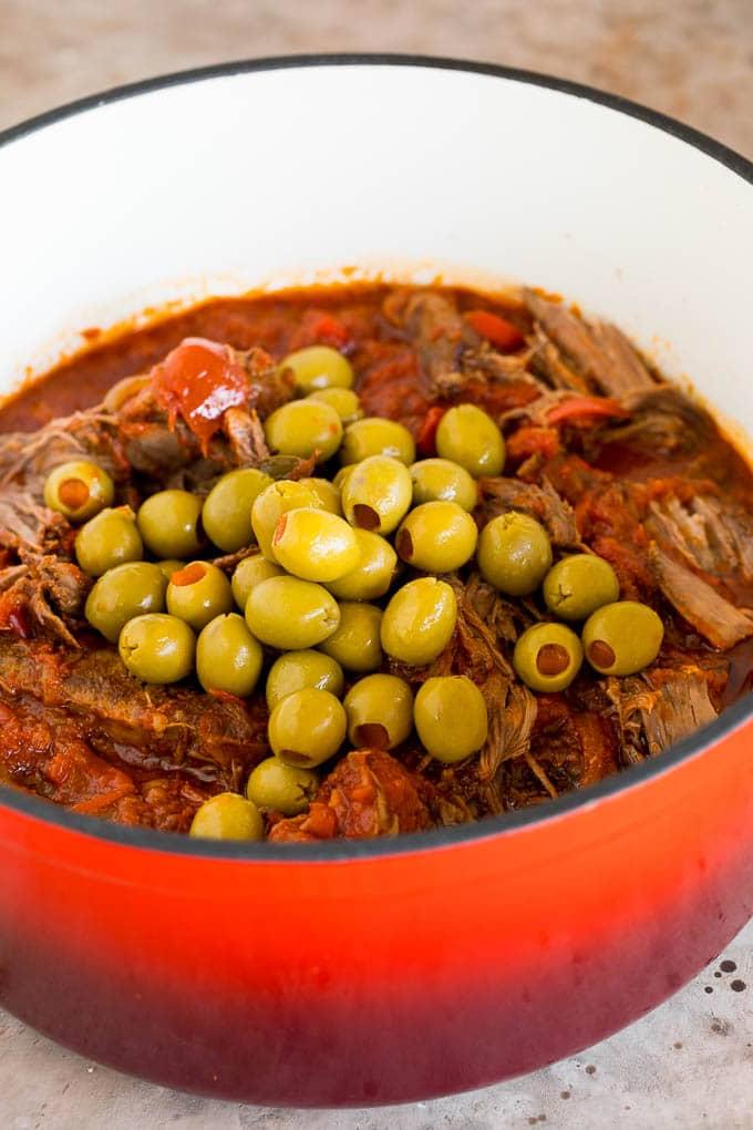 Dieses Ropa Vieja Rezept ist ein traditionelles Gericht aus Rinderbraten, das mit Tomaten und Gewürzen zart geschmort, dann zerzupft und mit Oliven serviert wird. Ein Topf mit zerzupftem Rindfleisch mit ganzen grünen Oliven darauf.