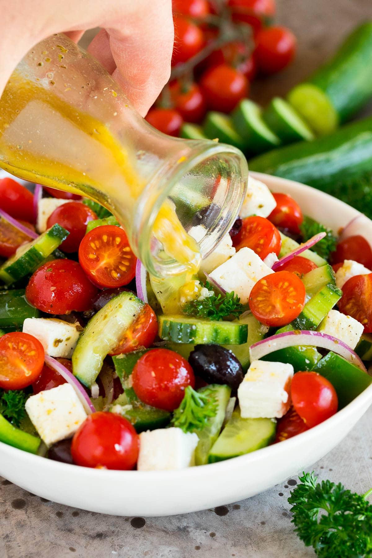 Griechisches Salatdressing 5 Griechisches Salatdressing wird über eine Schüssel mit gewürfeltem Gemüse wie Tomaten, Gurken und Oliven gegossen.