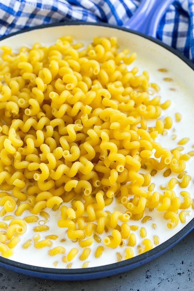 Pasta in Milch mit Gewürzen in einer Pfanne.