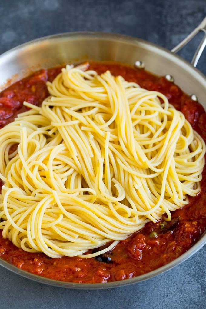 Spaghetti in einer Pfanne mit Tomatensauce, Oliven und Kapern.