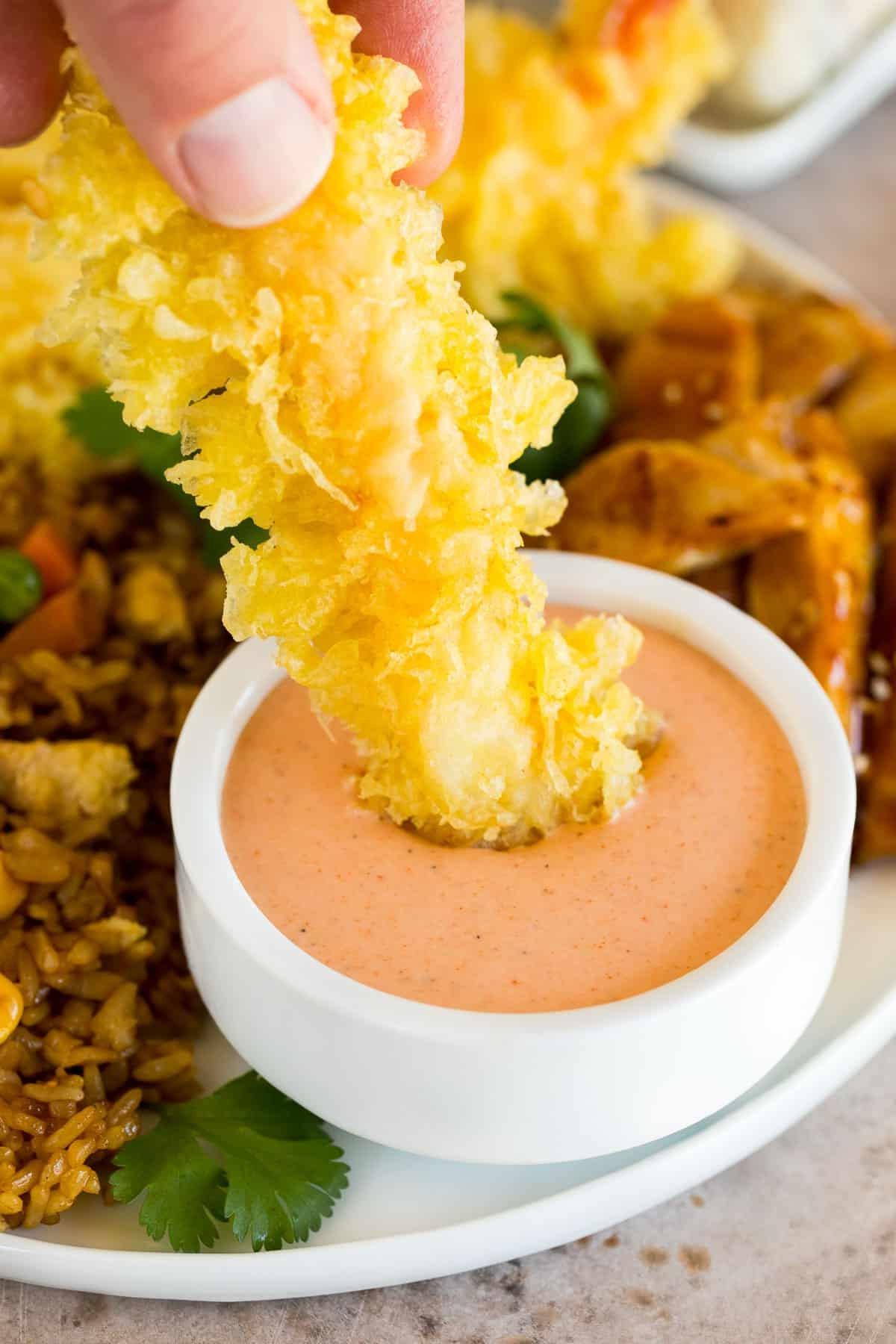 Yum Yum Sauce Rezept 6 Eine Hand, die eine Tempura-Garnele in Yum Yum Sauce taucht.