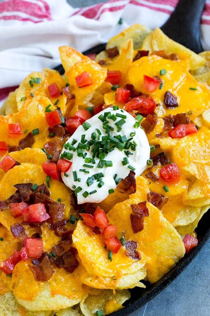 Irische Nachos Rezept | Kartoffel-Nachos | Kartoffelchip-Rezept | Vorspeisen-Rezept #nachos #kartoffeln #käse #speck #vorspeise #ahurt Eine Pfanne mit Irischen Nachos, belegt mit geschmolzenem Käse, Speck, Tomaten und Sauerrahm.