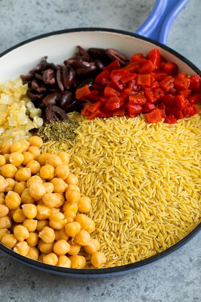 Orzo pasta, olives, chickpeas and roasted peppers in a skillet.