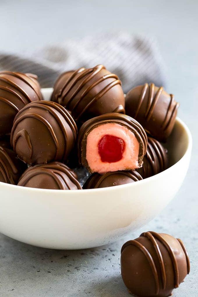 Schokolierte Kirschen Rezept | Kirsch-Pralinen | Kirsch-Bonbons #schokolade #süßigkeiten #dessert #kirsche #sweets #ahurt Eine Schüssel schokolierter Kirschen, eine davon aufgeschnitten.