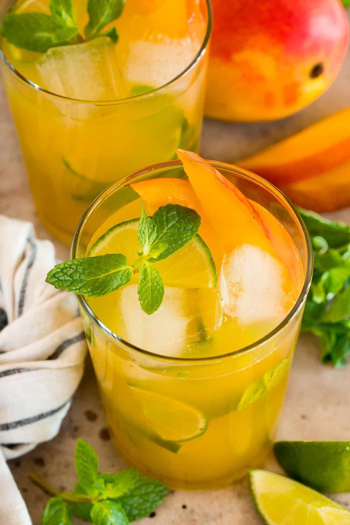 Mango Mojito 6 Gläser mit Mango Mojito, reichlich Eis, frischer Minze und saftigen Mangoscheiben. Nahaufnahme eines unwiderstehlich kühlen Cocktails.